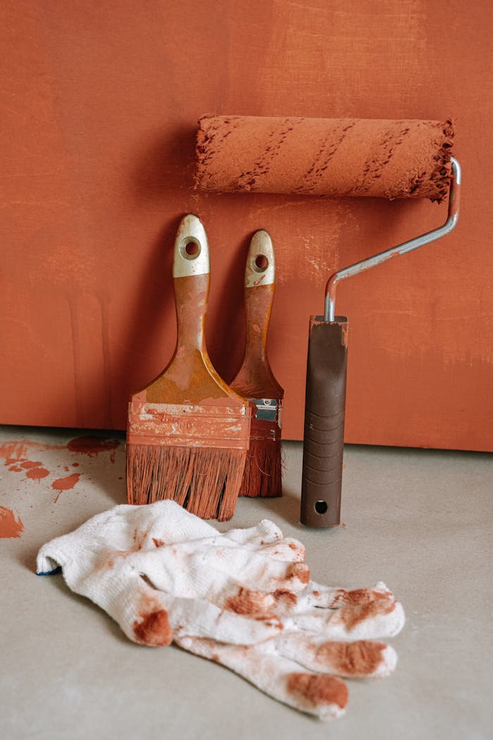 Painting tools including brushes and roller with brown paint stains on a flat surface.